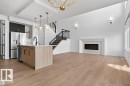 Spacious open-concept interior featuring light wood-finish flooring, a contemporary kitchen island with a white countertop and dark cabinetry, and a black metal staircase with wood treads - 19 Rosa Crescent, St. Albert, AB 