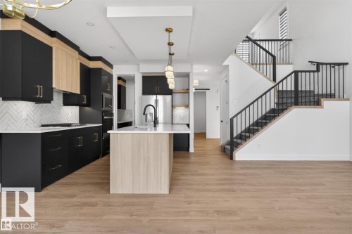 Modern kitchen featuring two-tone cabinetry with gold-finish hardware, a herringbone tile backsplash, and a central island with a waterfall countertop - 19 Rosa Crescent, St. Albert, AB 