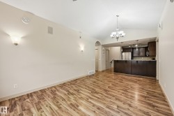 Open-concept living space featuring wood-finish flooring, vaulted ceilings, and an elegant chandelier - 