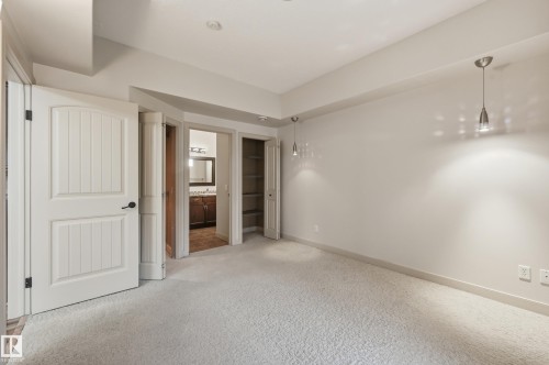 Carpeted interior space featuring light-colored walls and two contemporary pendant light fixtures - 50 2565 Hanna Crescent, Edmonton, AB 