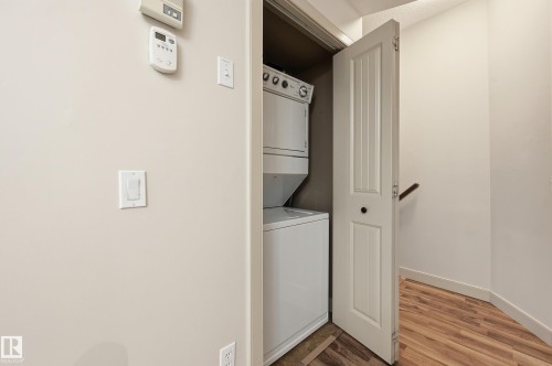 Dedicated laundry closet featuring a stacked white washer and dryer unit, wood-finish flooring, and a white paneled door - 50 2565 Hanna Crescent, Edmonton, AB 