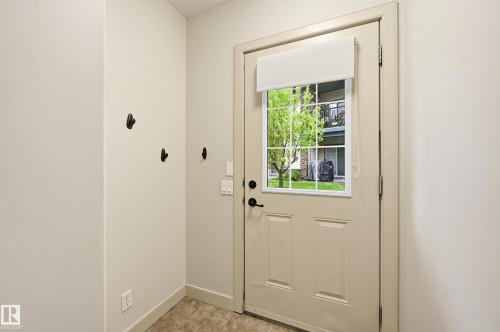 Entryway featuring a paneled door with a grid window, an opaque roll-up shade, and three wall-mounted hooks - 50 2565 Hanna Crescent, Edmonton, AB 