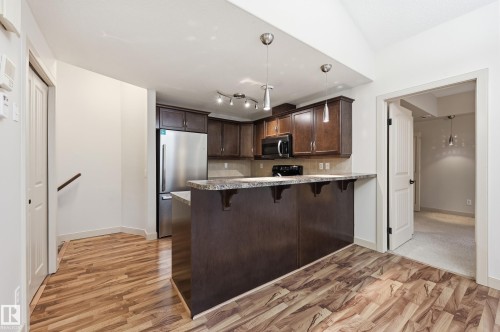 Kitchen featuring dark wood-finish cabinetry, stainless steel appliances, and a breakfast bar with stone-finish countertops - 50 2565 Hanna Crescent, Edmonton, AB 