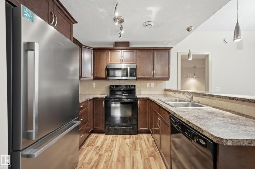U-shaped kitchen featuring dark wood cabinetry, a stainless steel refrigerator, black range, stainless steel microwave, and wood-finish flooring - 50 2565 Hanna Crescent, Edmonton, AB 