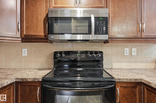 Kitchen featuring a black electric range, stainless steel microwave, light-toned tiled backsplash, wood-finish cabinetry, and laminate countertops - 50 2565 Hanna Crescent, Edmonton, AB 