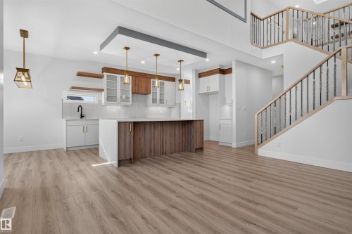 Open-concept living area featuring a kitchen island with wood-finish paneling, white shaker cabinetry, and light wood-finish flooring - 84 Rosa Crescent, St. Albert, AB - Indoor Photo Showing Kitchen