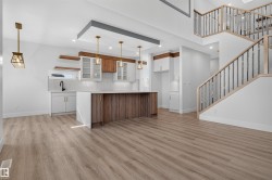 Open-concept living area featuring a kitchen island with wood-finish paneling, white shaker cabinetry, and light wood-finish flooring - 