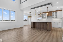 Open-concept living space featuring wood-finish flooring, a two-story ceiling, and a kitchen with an island, two-tone cabinetry, and pendant lighting - 