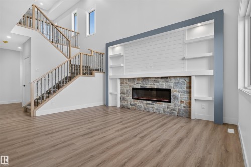 Open-concept living area featuring wood-finish flooring, a contemporary fireplace with a stone surround, built-in shelving, a modern staircase with wrought iron balusters, and abundant natural light from multiple windows - 84 Rosa Crescent, St. Albert, AB - Indoor With Fireplace