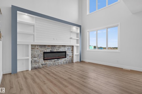 Living area featuring a stone-clad fireplace with an electric insert, built-in shelving with recessed lighting, shiplap detailing, and wood-finish flooring - 84 Rosa Crescent, St. Albert, AB - Indoor Photo Showing Living Room With Fireplace