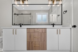 Dual vanity with white shaker-style cabinetry and a central wood-finish drawer stack, all featuring gold-tone hardware - 
