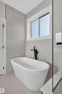Freestanding soaking tub with a matte black floor-mounted faucet, complemented by light-toned wall and floor tiling - 