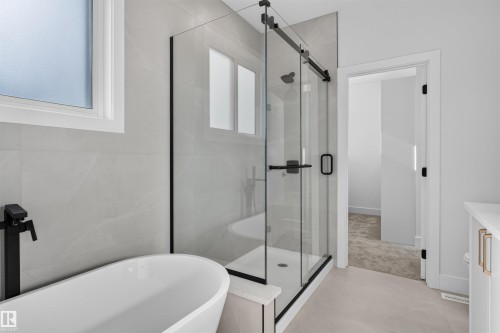 Contemporary bathroom featuring a freestanding tub with matte black fixtures, a frameless glass shower enclosure, large format tile walls, and light-toned flooring - 84 Rosa Crescent, St. Albert, AB - Indoor Photo Showing Bathroom