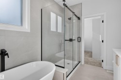 Contemporary bathroom featuring a freestanding tub with matte black fixtures, a frameless glass shower enclosure, large format tile walls, and light-toned flooring - 