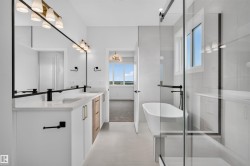 Modern bathroom featuring a dual vanity with white cabinetry, wood-finish accents, and black hardware - 