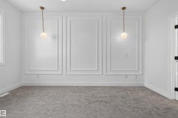 Interior room featuring decorative wall molding, two contemporary pendant light fixtures with spherical glass shades, and light gray carpeting - 