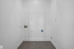 Dedicated laundry area featuring modern white paneling, dark tile flooring, and essential utility hookups - 