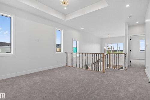 Spacious carpeted landing featuring a wood and metal spindle railing, multiple windows, recessed lighting, and a tray ceiling with a central lighting fixture - 84 Rosa Crescent, St. Albert, AB - Indoor Photo Showing Other Room