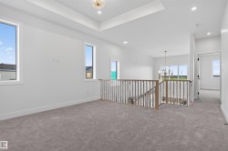 Spacious carpeted landing featuring a wood and metal spindle railing, multiple windows, recessed lighting, and a tray ceiling with a central lighting fixture - 