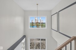Two-story foyer with a gold-tone chandelier, upper-level accent windows, and a light wood and black metal baluster railing - 