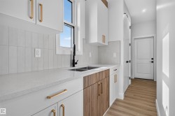Modern kitchen space featuring white cabinetry with gold hardware, a dual basin sink with a black faucet, light-toned countertops, and wood-finish flooring - 