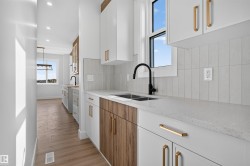 Kitchen featuring white cabinetry, wood-finish accent cabinetry, light countertops, black faucet, and vertical tile backsplash - 