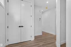 Hallway featuring wood-finish flooring, recessed lighting, and contemporary white doors with matte black hardware - 