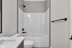 Bathroom featuring a white tub/shower combination with matte black fixtures, a white toilet, and a vanity with a white countertop and integrated sink - 