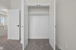 Recessed closet with a single hanging rod and upper shelf, featuring white walls and grey carpet flooring - 