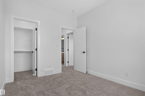 Carpeted room featuring a built-in closet with shelving and hanging rod, white walls, white trim, and modern black hardware - 84 Rosa Crescent, St. Albert, AB - Indoor Photo Showing Other Room