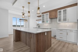 Contemporary kitchen featuring a large island with a light-toned countertop, wood-finish base cabinetry, and brass-toned hardware - 