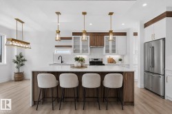 Spacious kitchen featuring a central island with countertop seating, modern white and wood-finish cabinetry, stainless steel appliances, and sleek pendant lighting - 