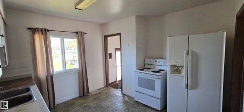 Kitchen featuring white wall paint, a double window with a dark curtain rod, white appliances, and a double basin stainless steel sink - Vegreville, AB - Indoor Photo Showing Kitchen