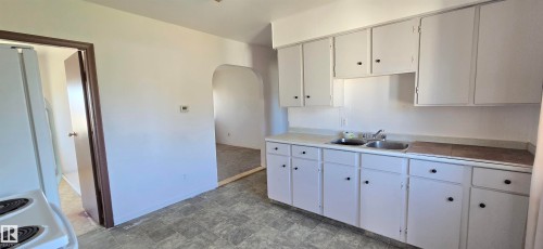 Kitchen featuring white cabinetry with black hardware, a double basin stainless steel sink, and light-toned countertops - Vegreville, AB - Indoor Photo Showing Kitchen With Double Sink