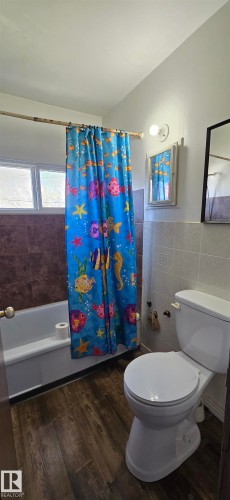 Bathroom featuring wood-finish flooring, a white bathtub, and a window with frosted glass - Vegreville, AB - Indoor Photo Showing Bathroom