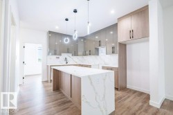 Modern kitchen featuring a large island with a waterfall countertop, sleek cabinetry, wood-finish flooring, and contemporary pendant lighting - 
