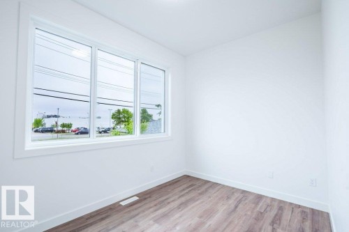 Bright interior room featuring a large triple-pane window, white walls, and wood-finish flooring - 5211 104A Street, Edmonton, AB 