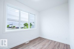 Bright interior room featuring a large triple-pane window, white walls, and wood-finish flooring - 
