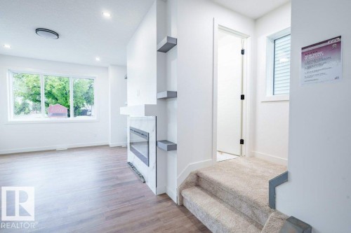 Open concept interior featuring wood-finish flooring, a contemporary fireplace with a stone-look surround, recessed lighting, and a large picture window - 5211 104A Street, Edmonton, AB 