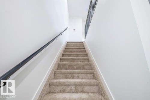 Carpeted staircase with light-toned walls and a black metal handrail - 5211 104A Street, Edmonton, AB 