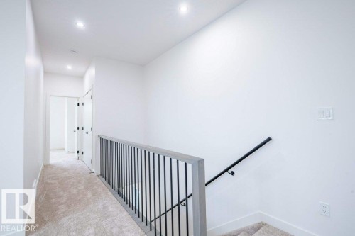 Upper-level hallway with neutral carpet, white walls, recessed lighting, and a modern stair railing with dark metal spindles and a wood-finish top rail - 5211 104A Street, Edmonton, AB 