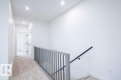 Upper-level hallway with neutral carpet, white walls, recessed lighting, and a modern stair railing with dark metal spindles and a wood-finish top rail - 