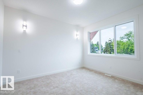 Room featuring a large triple-pane window, neutral carpet flooring, white walls, and two wall-mounted sconce light fixtures - 5211 104A Street, Edmonton, AB 