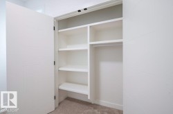Integrated closet system featuring white bi-fold doors with horizontal grooves, multiple white shelving units, a clothing rod, and neutral-toned carpeting - 