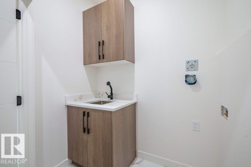 Utility room featuring wood-finish cabinetry with matte black hardware, a stainless steel sink, and white countertop - 5211 104A Street, Edmonton, AB 