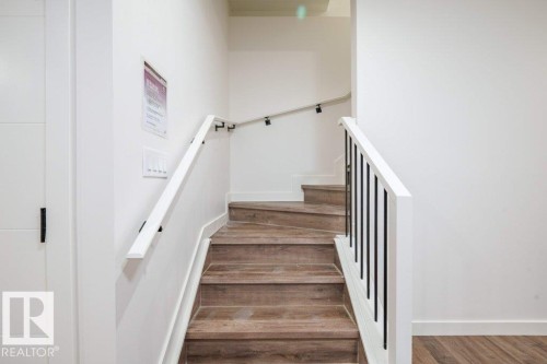 Staircase featuring wood-finish treads, white risers, and a contemporary railing with white balusters and black spindles - 5211 104A Street, Edmonton, AB 