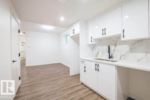 Kitchenette featuring white high-gloss cabinetry, quartz-finish countertops, and a full-height backsplash with a marble-effect pattern - 5211 104A Street, Edmonton, AB 