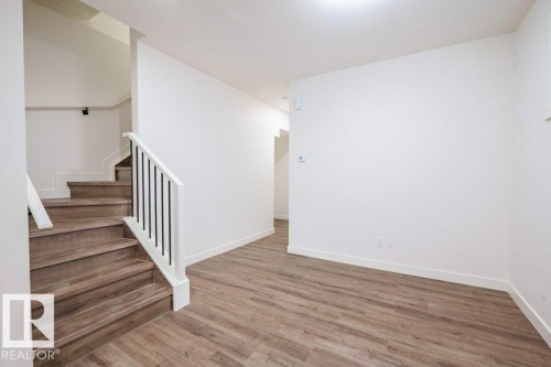 Entryway featuring wood-finish flooring, white walls, and a staircase with white risers, wood treads, and a white handrail with black vertical balusters - 5211 104A Street, Edmonton, AB 