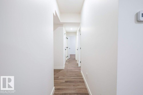 Hallway featuring wood-finish flooring, crisp white walls, and contemporary black door hardware - 5211 104A Street, Edmonton, AB 