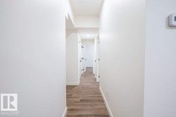 Hallway featuring wood-finish flooring, crisp white walls, and contemporary black door hardware - 